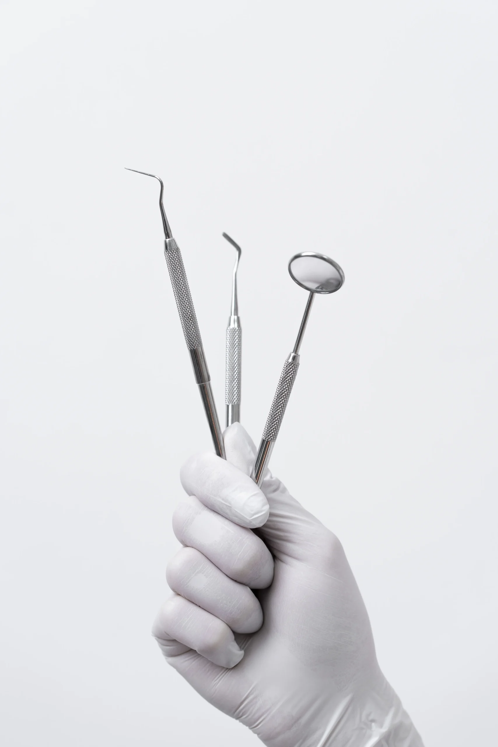 Main tenant des instruments dentaires : miroir, sonde et excavateur.